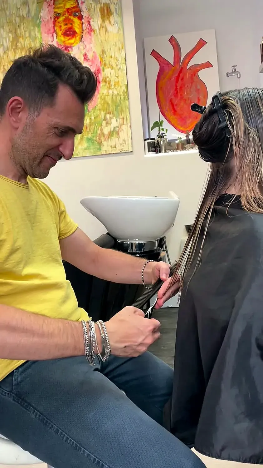 Matteo al lavoro vicino al lavandino bianco, con i quadri colorati del salone sullo sfondo