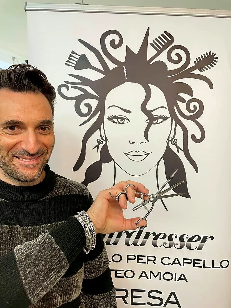 Matteo Amoia sorride con le forbici in mano davanti al disegno del salone
